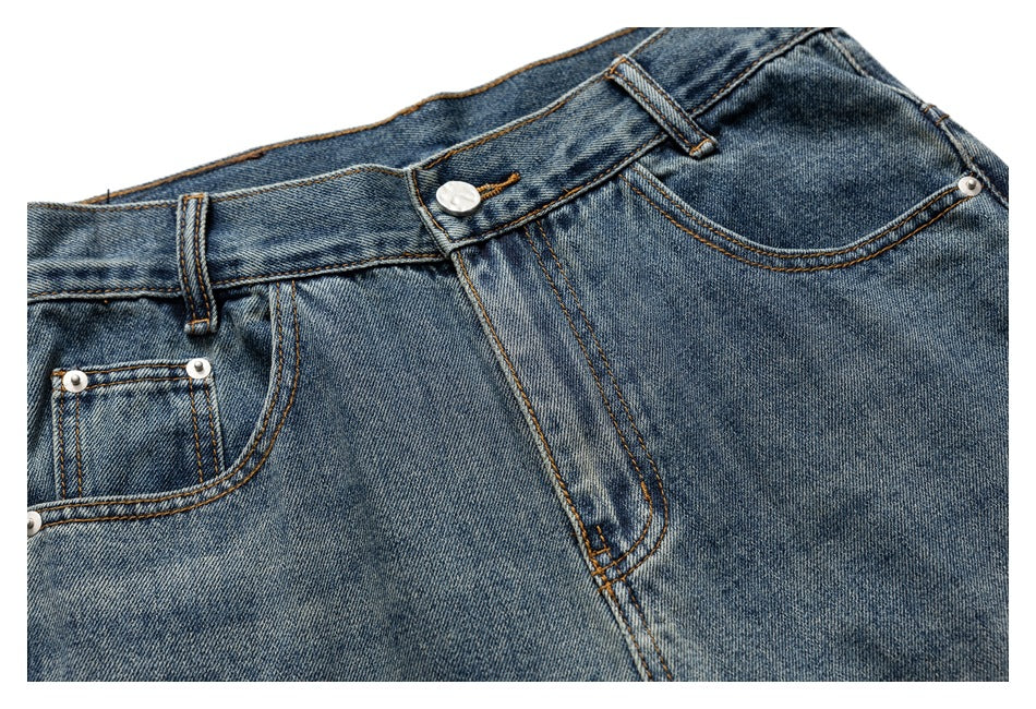Cropped front view of blue-wash jeans showing the waistband, button, fly and front pockets.