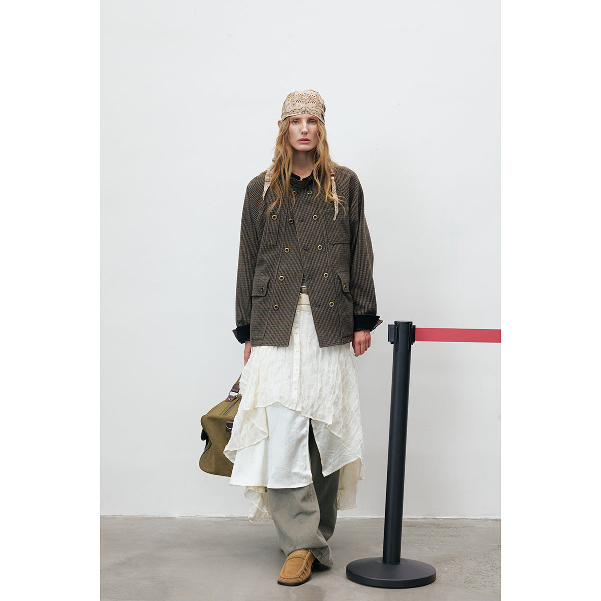 Full-length view of a model in a dark checked jacket, layered white skirt, gray trousers, and tan shoes.