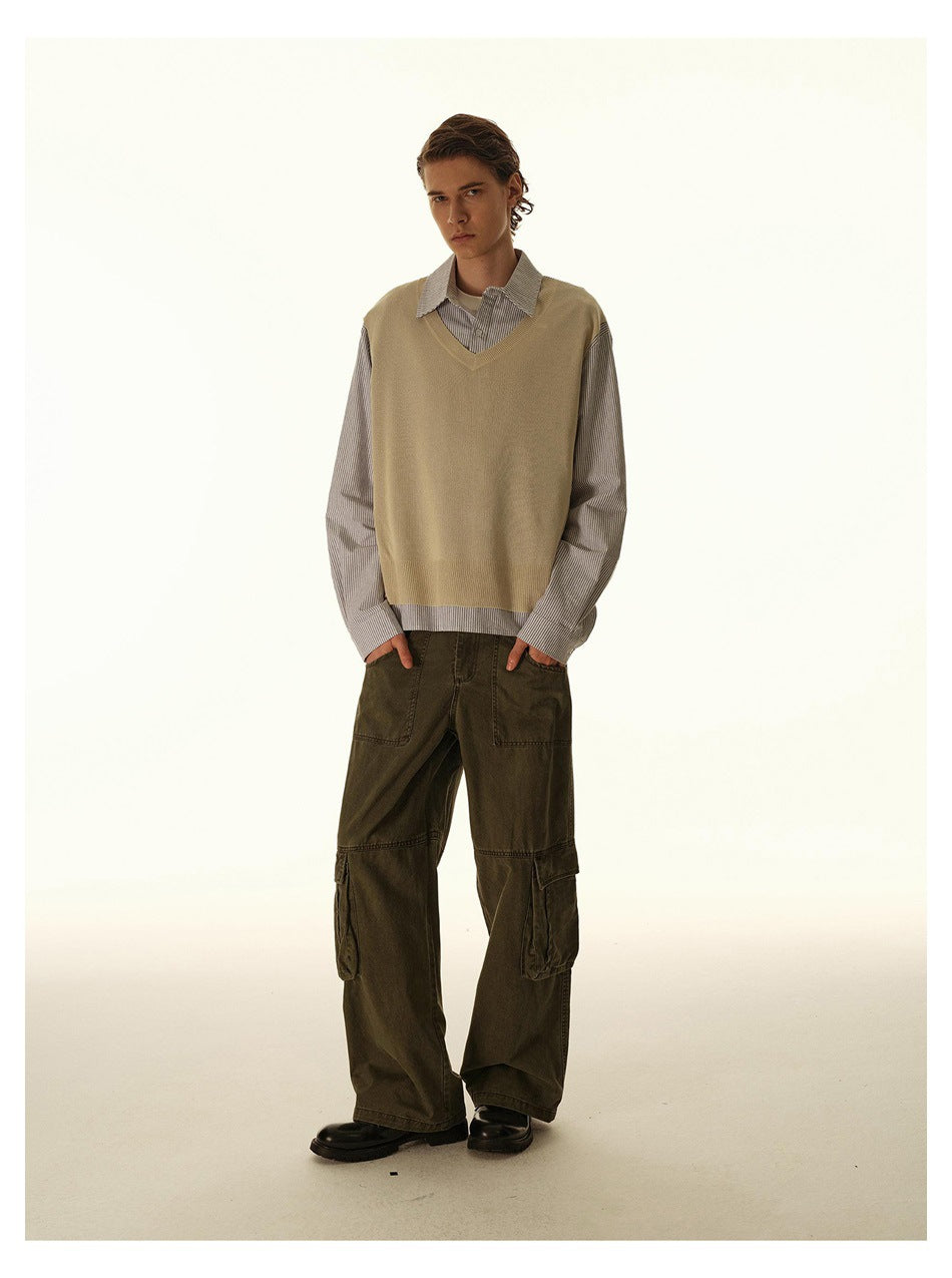 Full-length model wearing a tan V-neck sweater vest, gray striped shirt, and loose dark olive cargo pants.