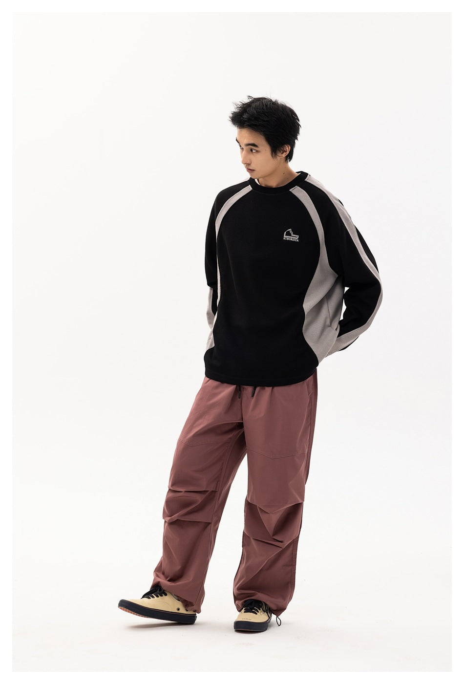 Model wearing black and gray panelled crew-neck sweatshirt with mauve wide-leg pants, full-length view
