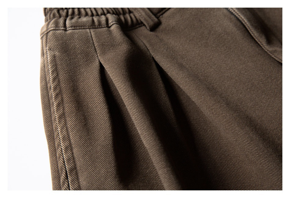 Close-up of the dark brown trousers' elastic waistband, belt loop, pleat, and pocket opening.