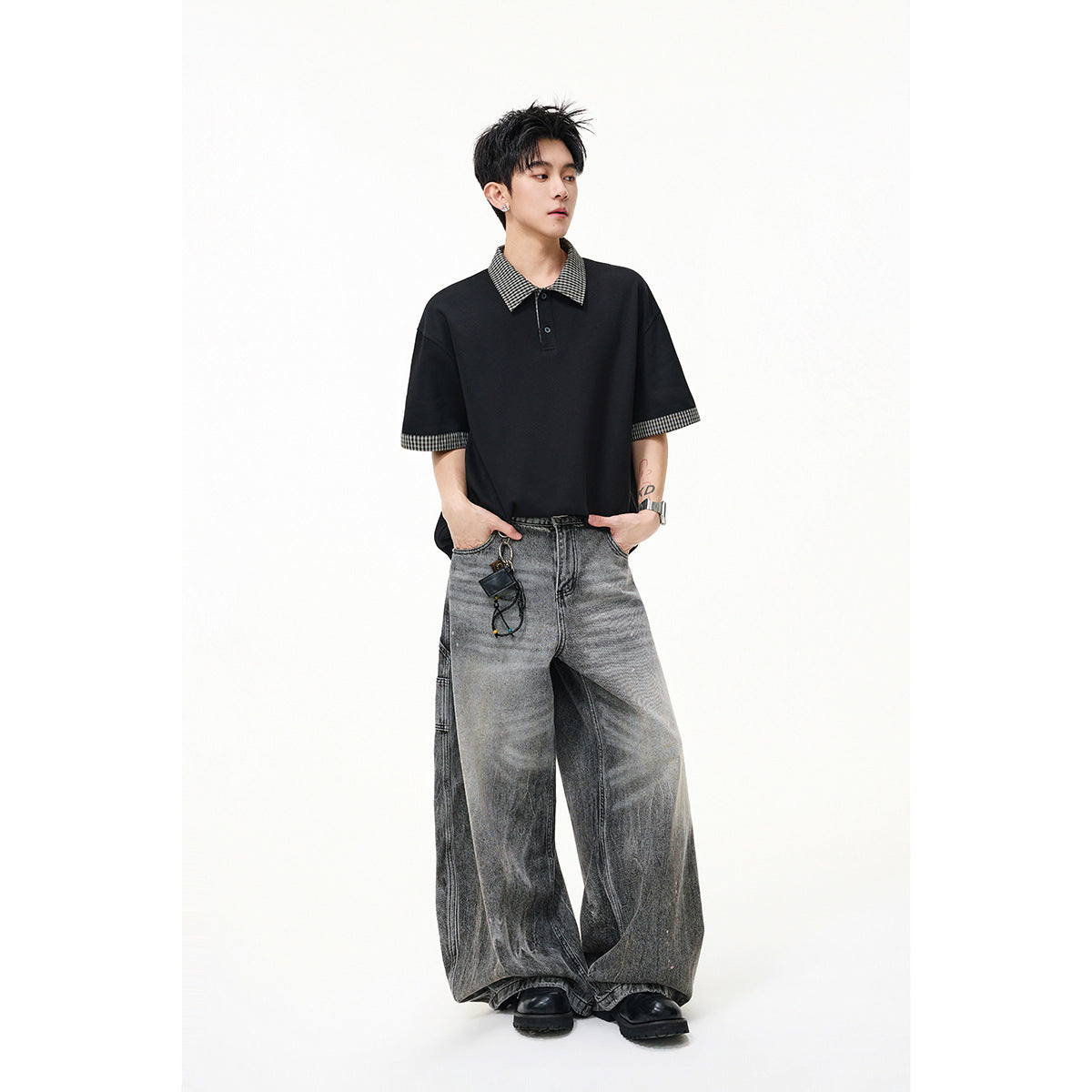Model wearing a black short-sleeve polo with checked collar and cuffs, paired with wide gray jeans.