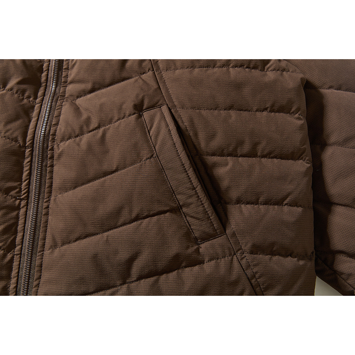 Close-up of a brown quilted jacket’s diagonal pocket opening and front zipper.