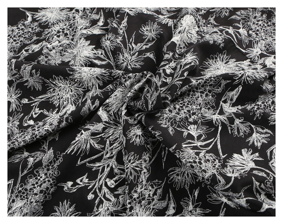 Close-up of draped black fabric with a dense white botanical and floral line pattern.