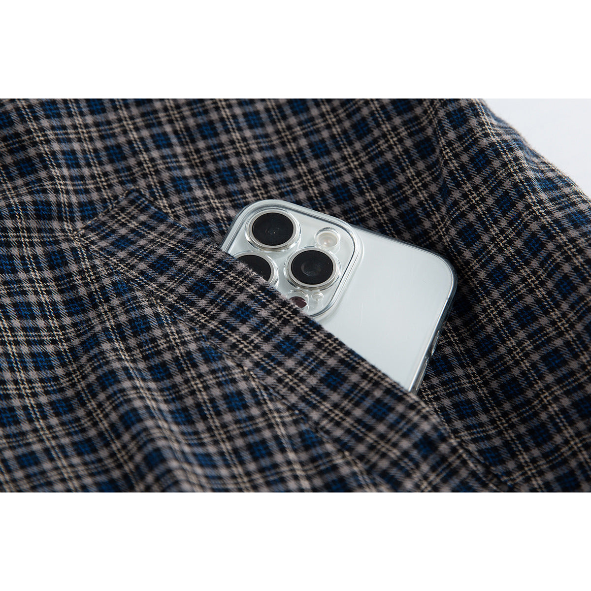 Close-up of a pocket in navy, gray and tan plaid fabric with a silver smartphone tucked inside.