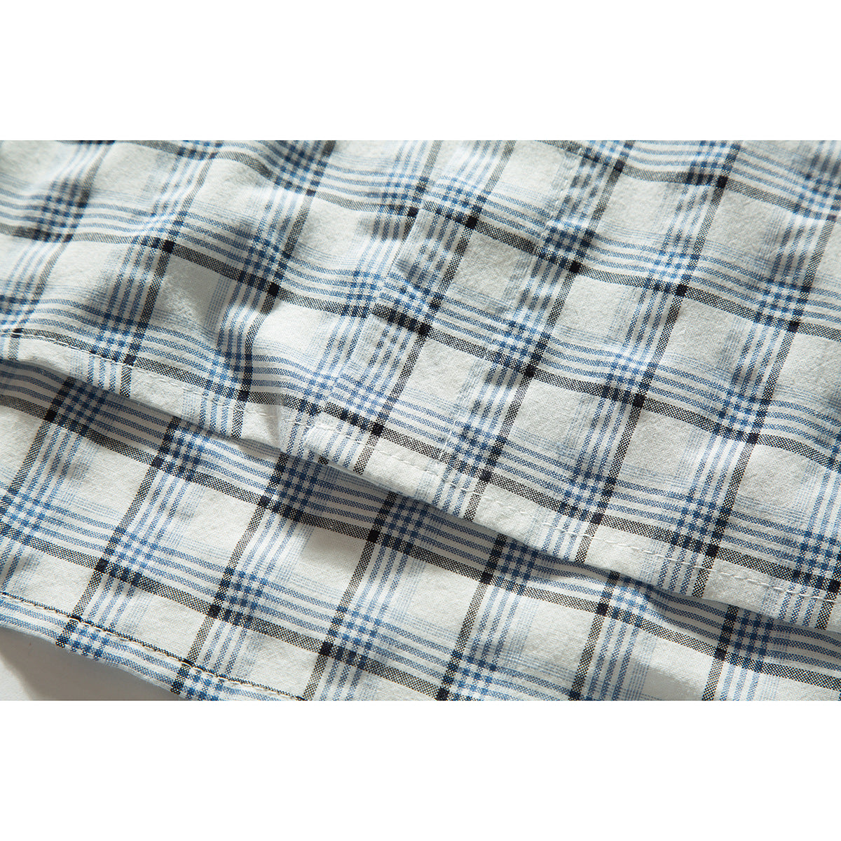 Close-up of white fabric with a blue and charcoal plaid pattern and a folded seam.