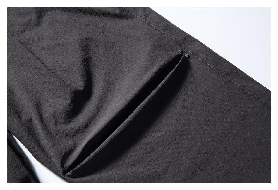Close-up of a charcoal pant leg showing a pleated side panel secured with two small snaps.