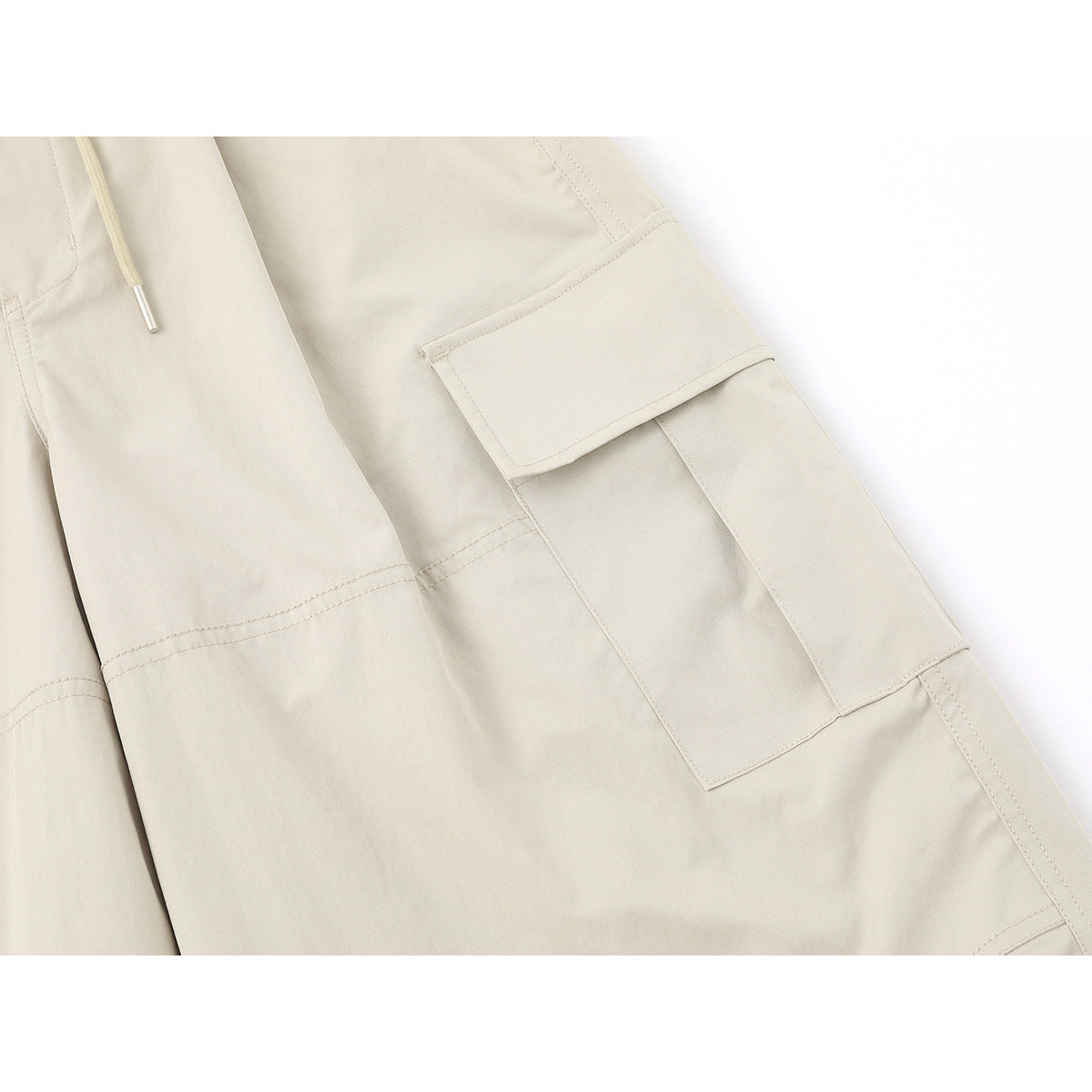 Close-up of light beige cargo pants showing a flap cargo pocket, drawstring tip and panel stitching.