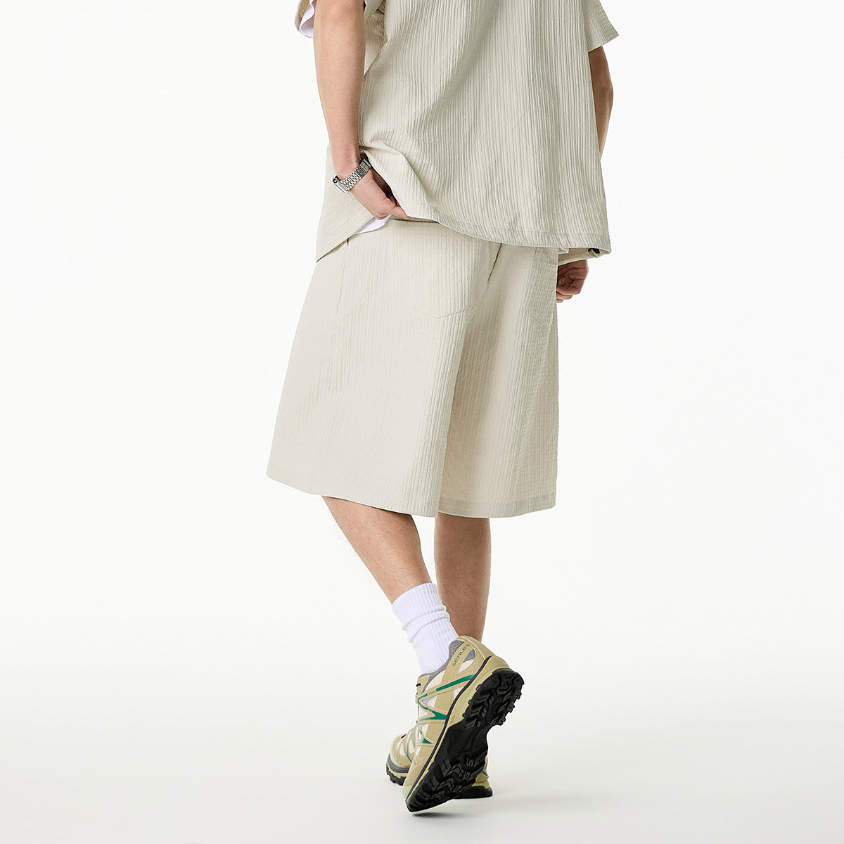 Cropped rear three-quarter view of a model wearing a light beige textured shirt and matching knee-length shorts.
