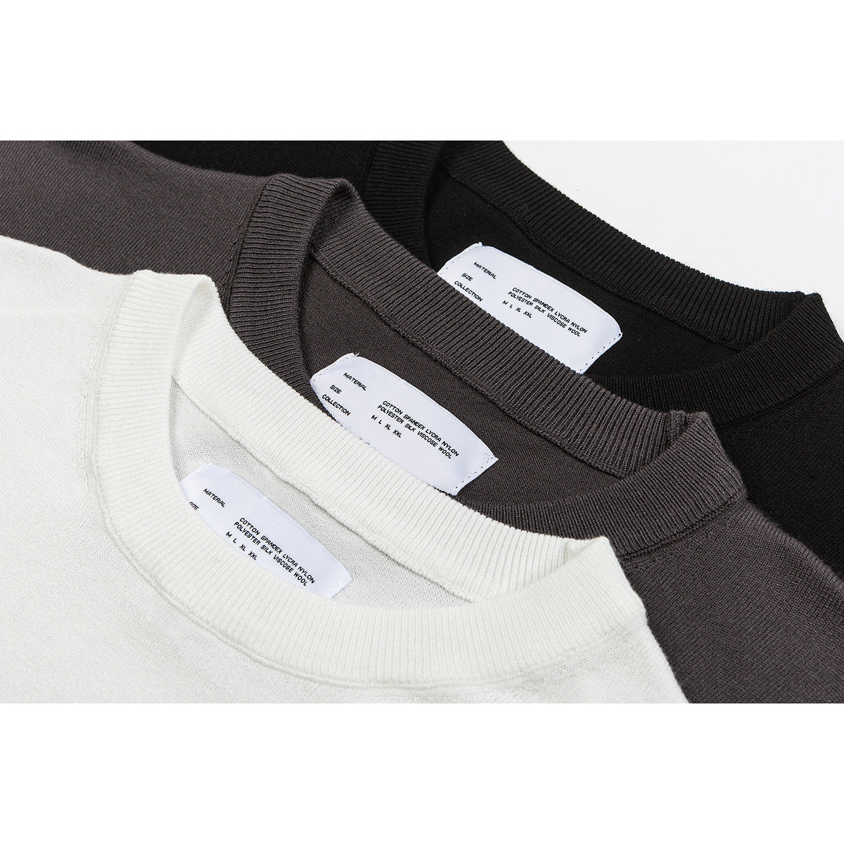 Close-up of cream, taupe and black knit tops showing ribbed crew necks and white inner labels.