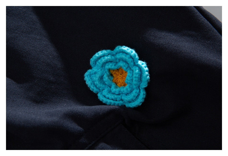 Extreme close-up of a turquoise crocheted flower with a yellow center on dark navy fabric.