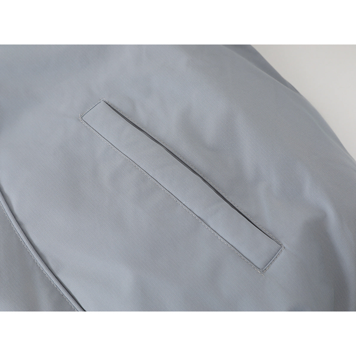Close-up of a slanted welt pocket on a light gray jacket.