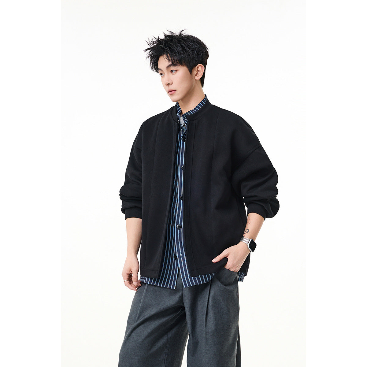 Model wearing a black oversized jacket over a blue striped shirt, with dark gray wide-leg trousers.