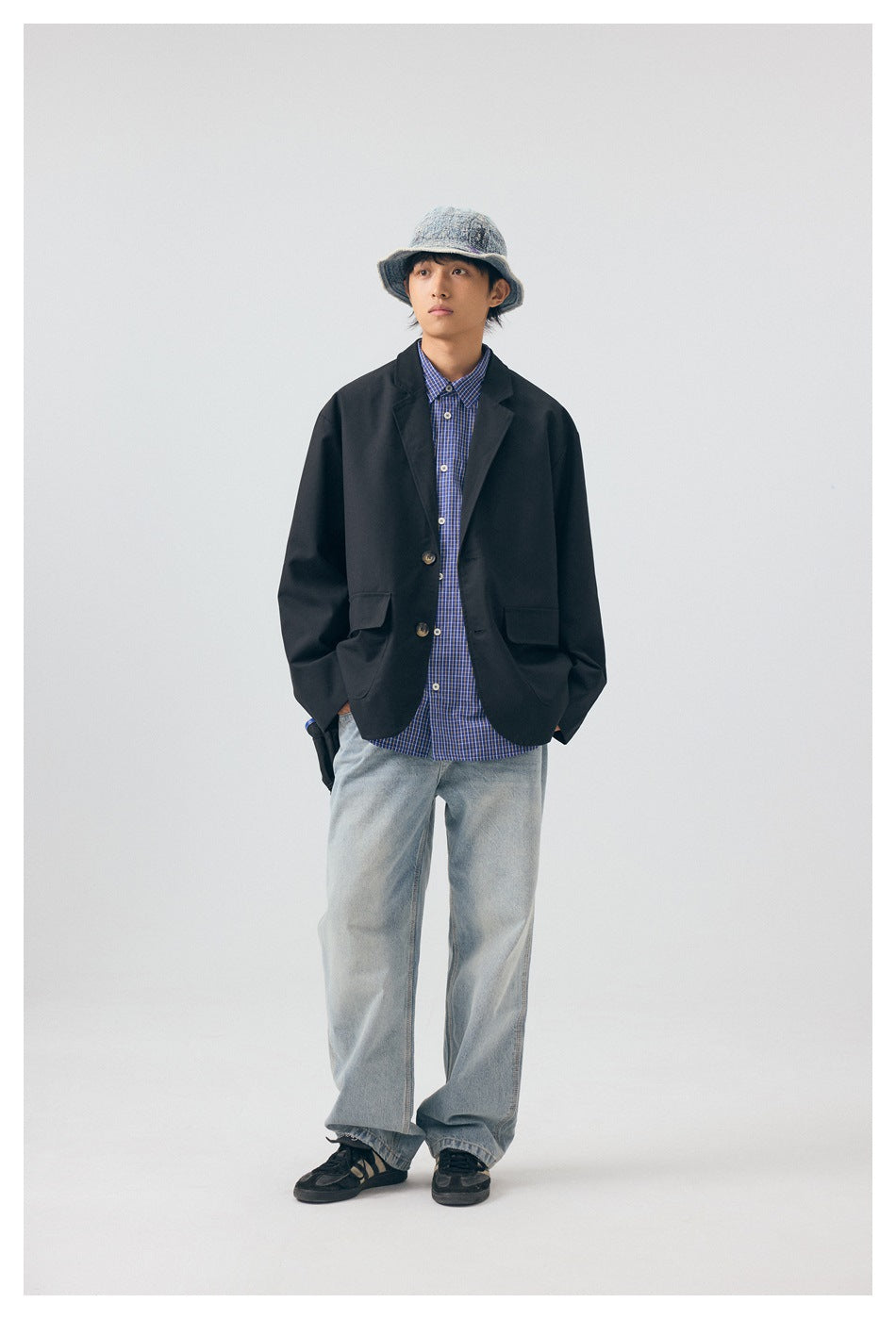 Model wearing black oversized blazer jacket over a blue plaid shirt with light jeans and a denim bucket hat