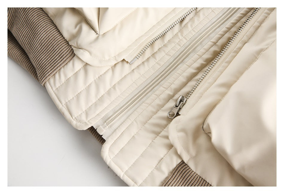Close-up of a cream jacket's quilted panels, several zippers, and taupe ribbed trim.