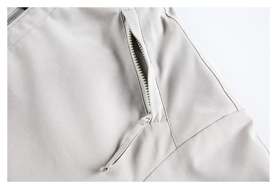 Close-up of a light gray jacket with a partially open vertical zip pocket and stitched panels.