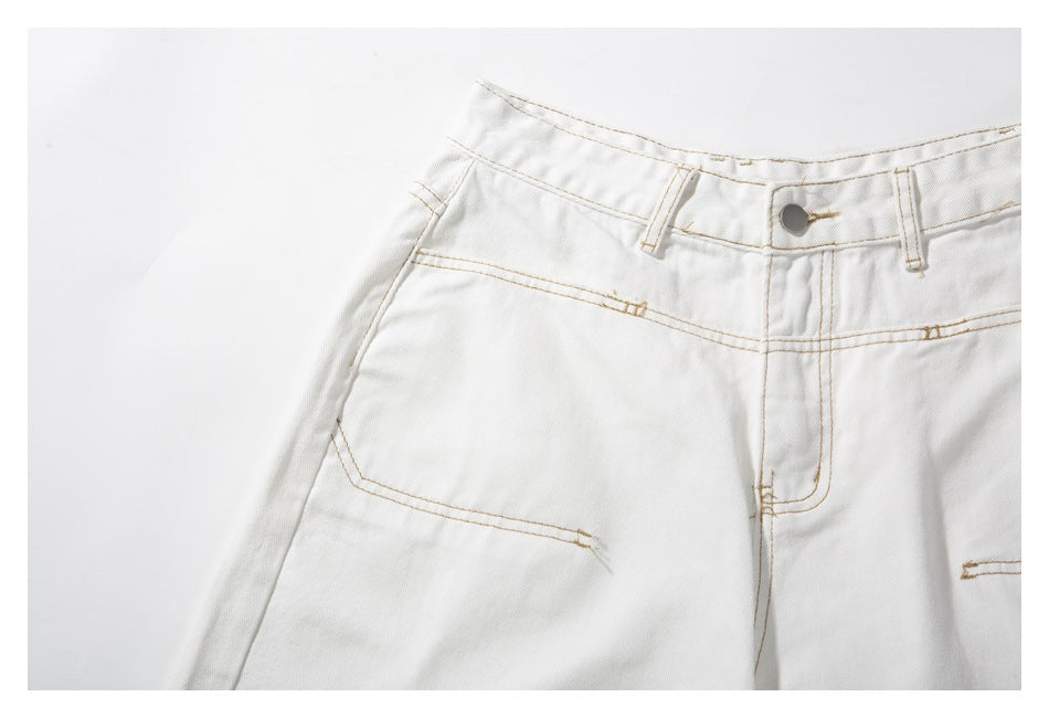 Close-up of white trousers showing the front waistband, metal button, belt loops, fly and tan stitching.