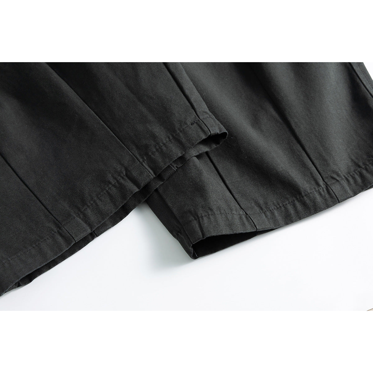 Close-up of the wide trouser legs and stitched hems in dark charcoal fabric.