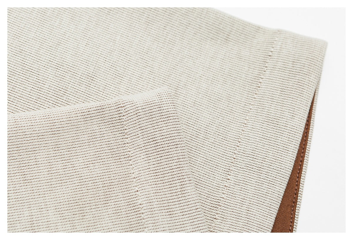 Close-up of a cream ribbed garment edge with brown trim and stitching.