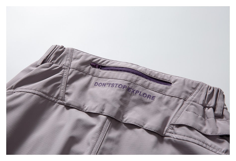 Pale mauve trouser waistband with a purple zip pocket and embroidered “DON'T STOP EXPLORE” text.