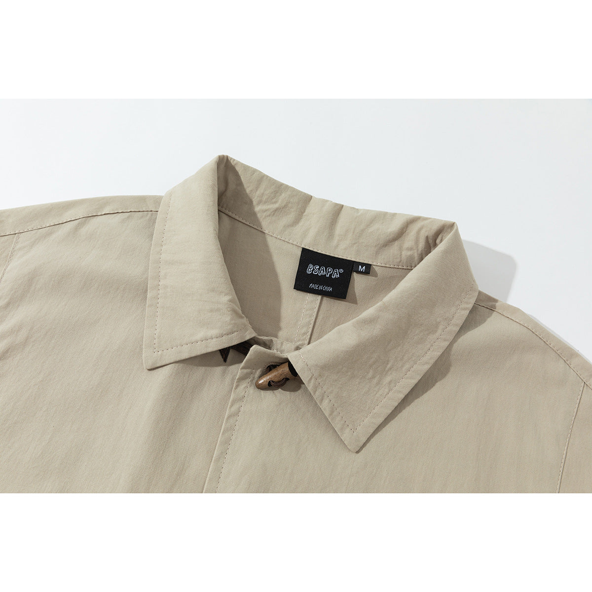 Close-up of a beige collared jacket with a brown toggle closure and a black neck label.