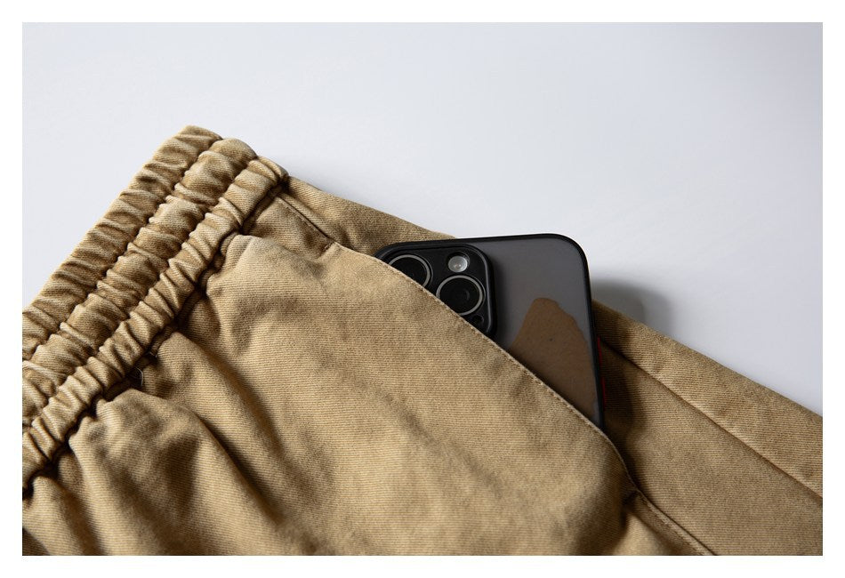 Close-up of tan shorts with an elastic waistband and a phone tucked into the front pocket.