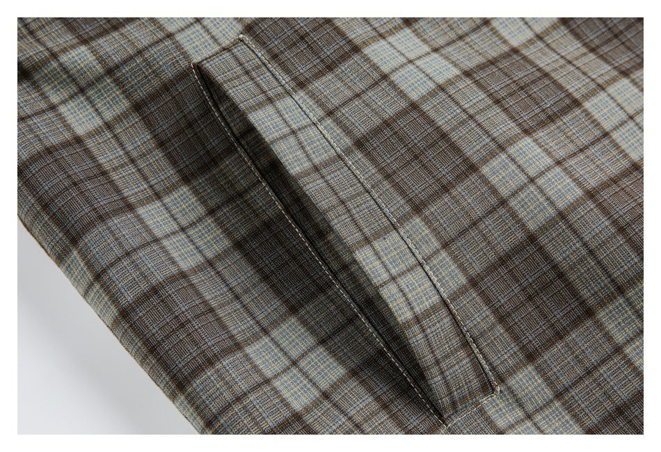 Close-up of a narrow welt pocket set into brown, blue, and tan plaid jacket fabric.