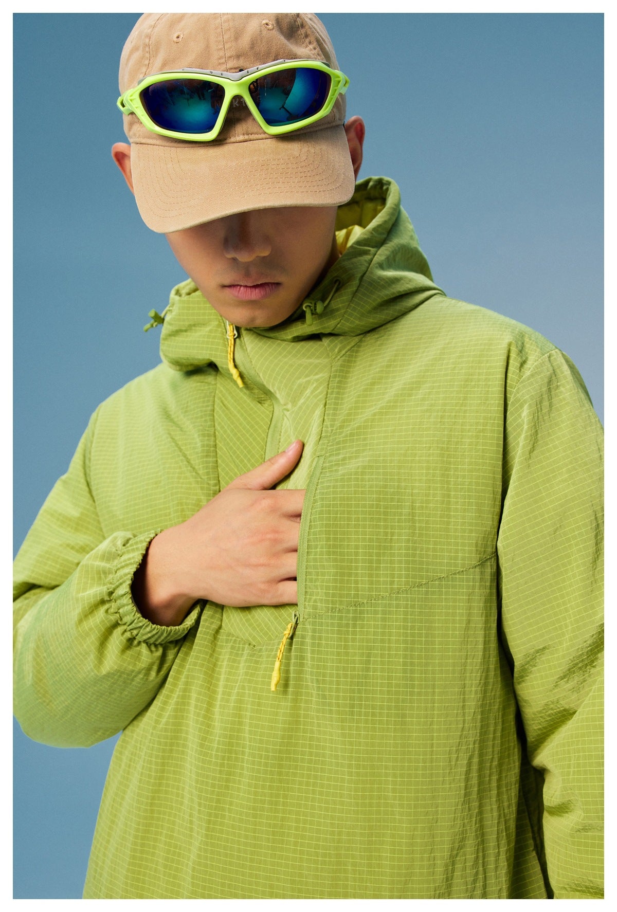 Close front view of a model wearing a lime green grid-pattern hooded jacket with a yellow-trimmed zipper.