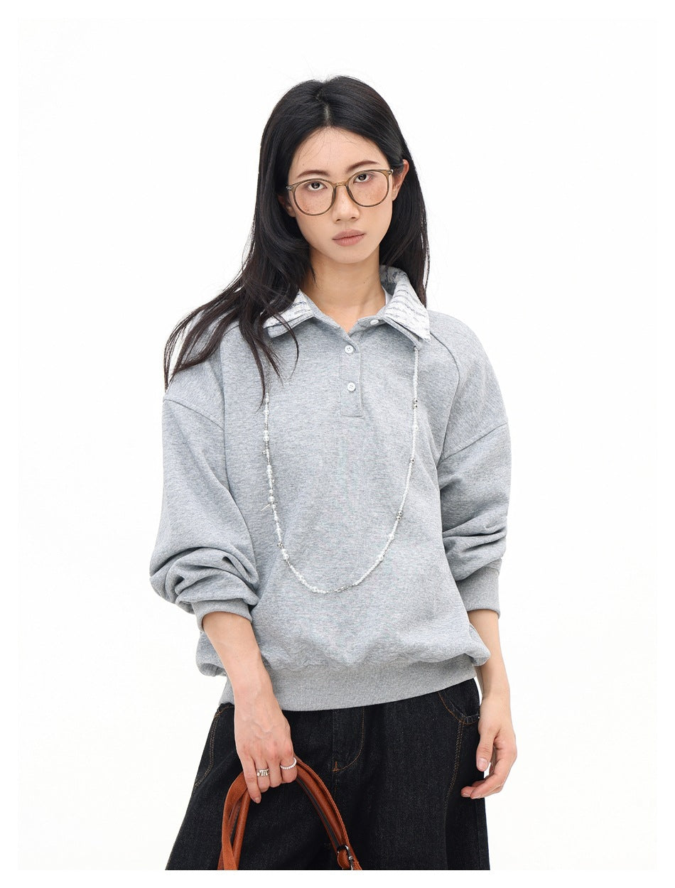 Model wearing a light gray oversized pullover with a striped collar and short button placket.