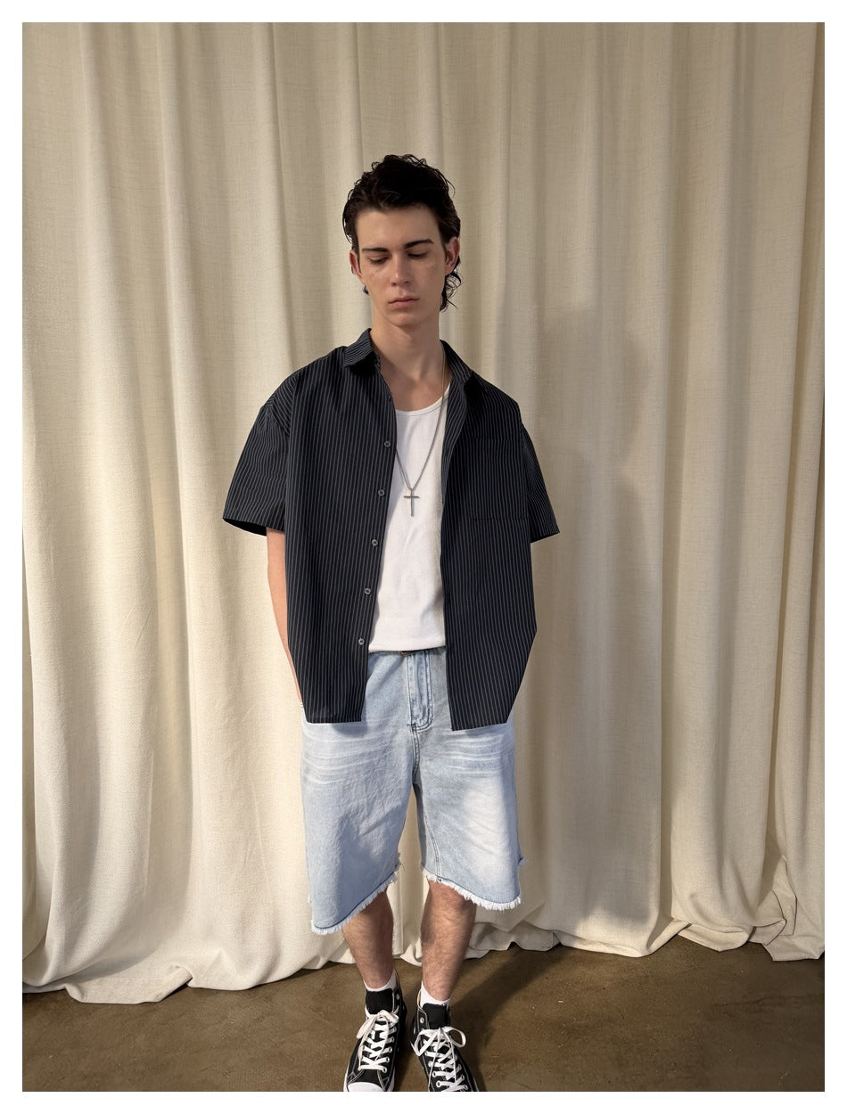 Front view of a model wearing a dark pinstriped short-sleeve shirt over a white tank and light blue frayed denim shorts.