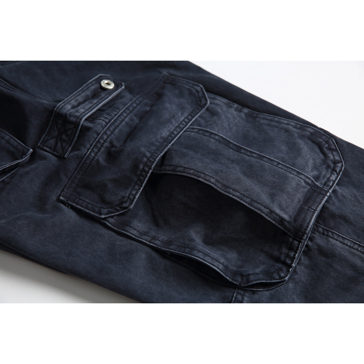 Close-up of dark navy cargo pants showing layered flap pockets, a metal button, and double stitching.
