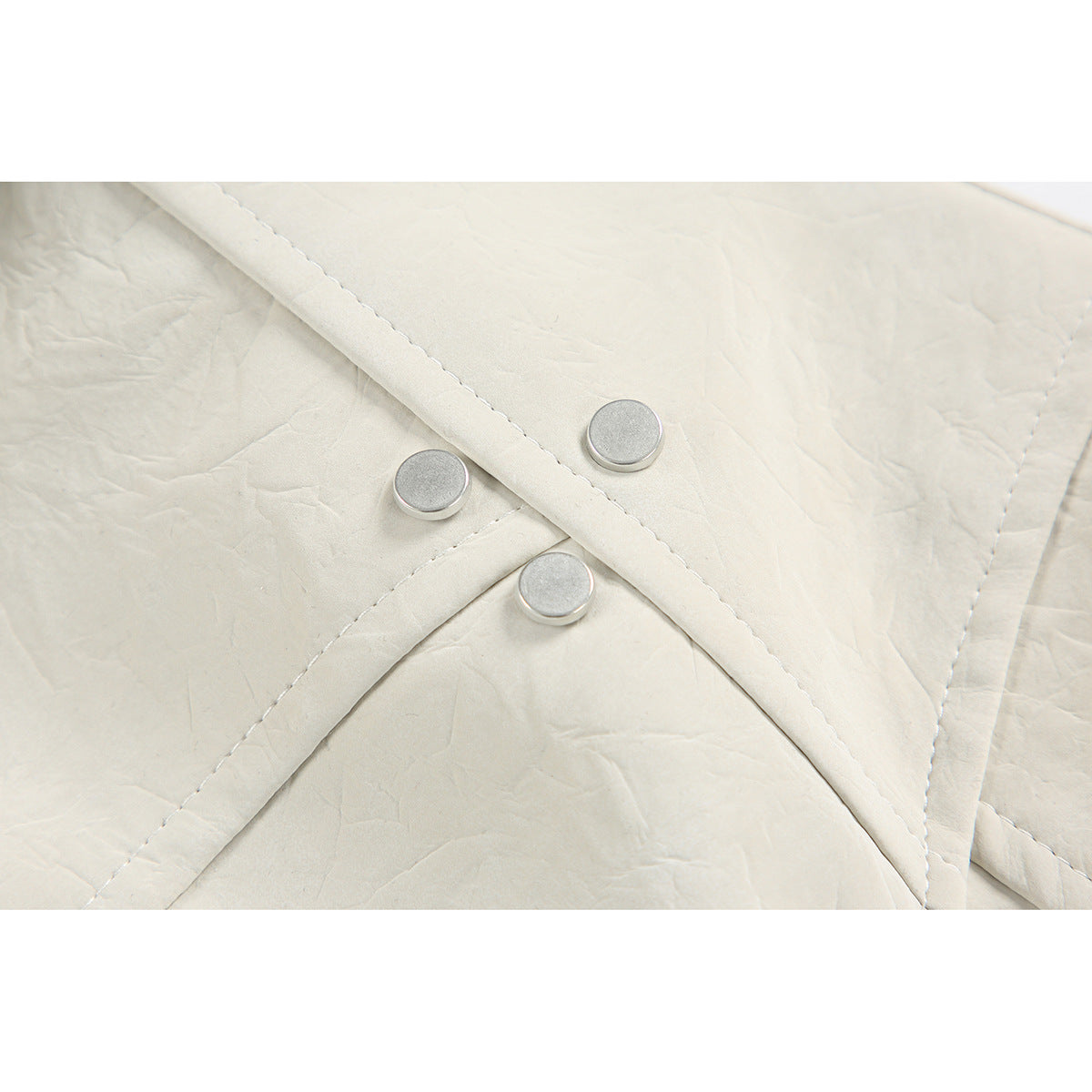 Close-up of an ivory jacket's overlapping front placket with three round silver snaps.