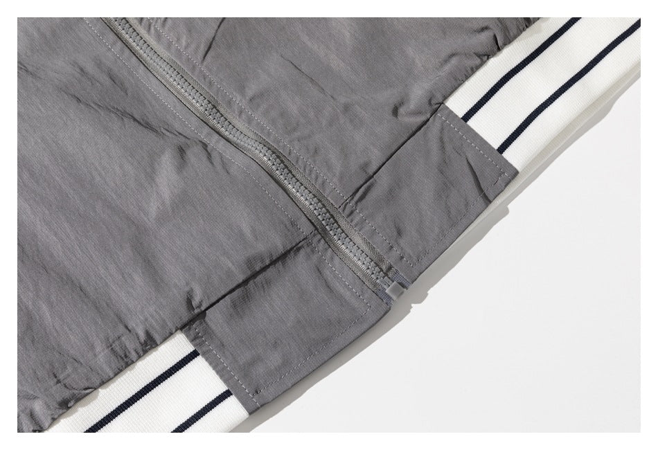 Close-up of a gray jacket zipper and white ribbed hem with two dark stripes.