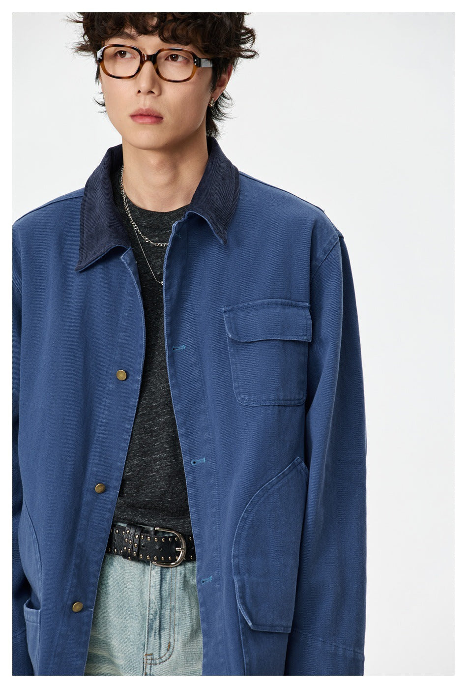 Close front view of a blue work jacket on a model, showing its dark collar, button placket and chest pocket.