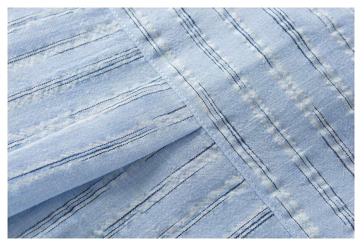 Close-up of pale blue fabric with narrow navy stripes, folded layers, and a stitched edge.