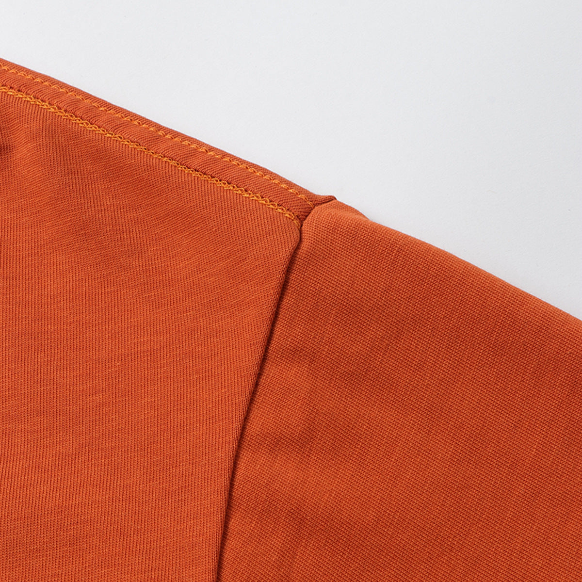 Close-up of an orange T-shirt shoulder seam and sleeve fabric.