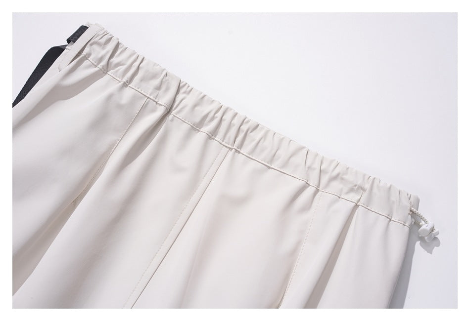 Close-up of a white garment’s gathered elastic waistband, with a black loop and drawcord toggle.