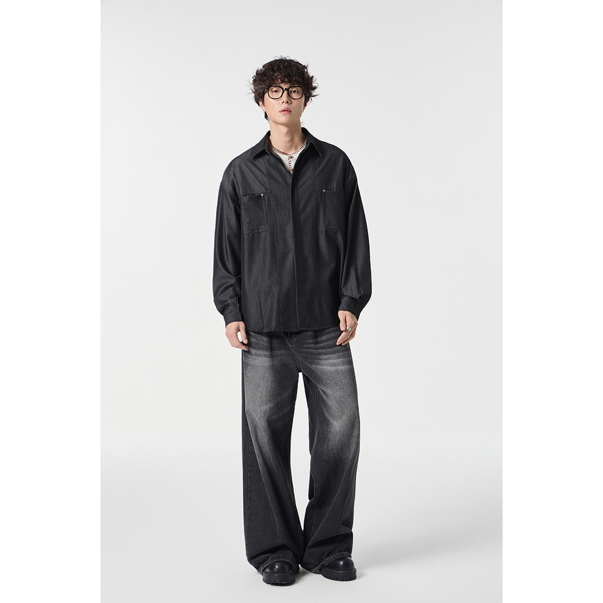 Full-length view of a model wearing a charcoal button-front shirt with chest pockets and washed black wide-leg jeans.