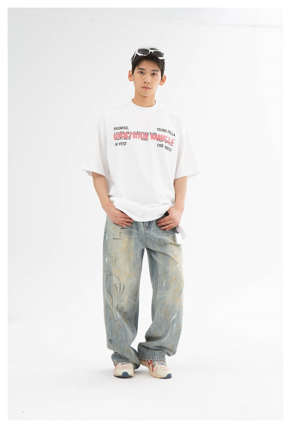 Full-length model wearing a white graphic T-shirt, loose distressed light-wash jeans, and sneakers.