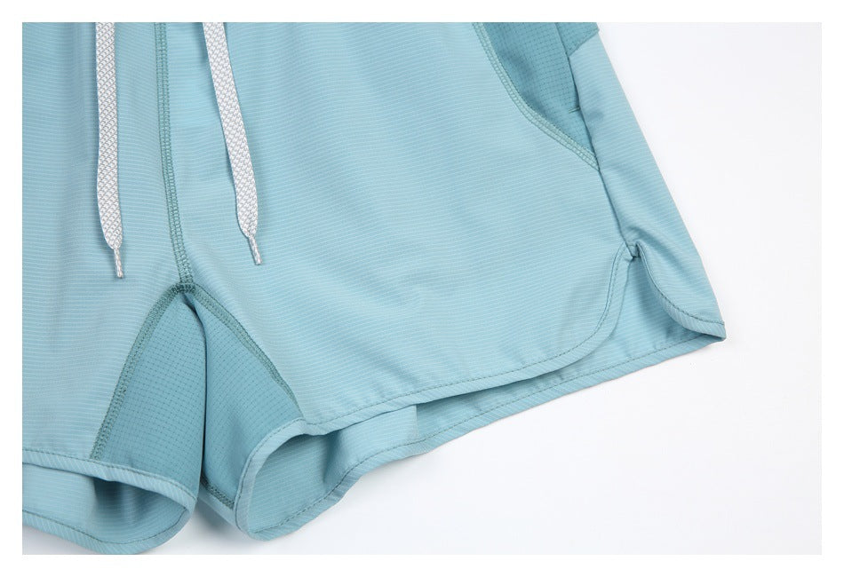 Close-up of aqua shorts showing the curved overlapping hem, inner panel, and patterned drawcords.