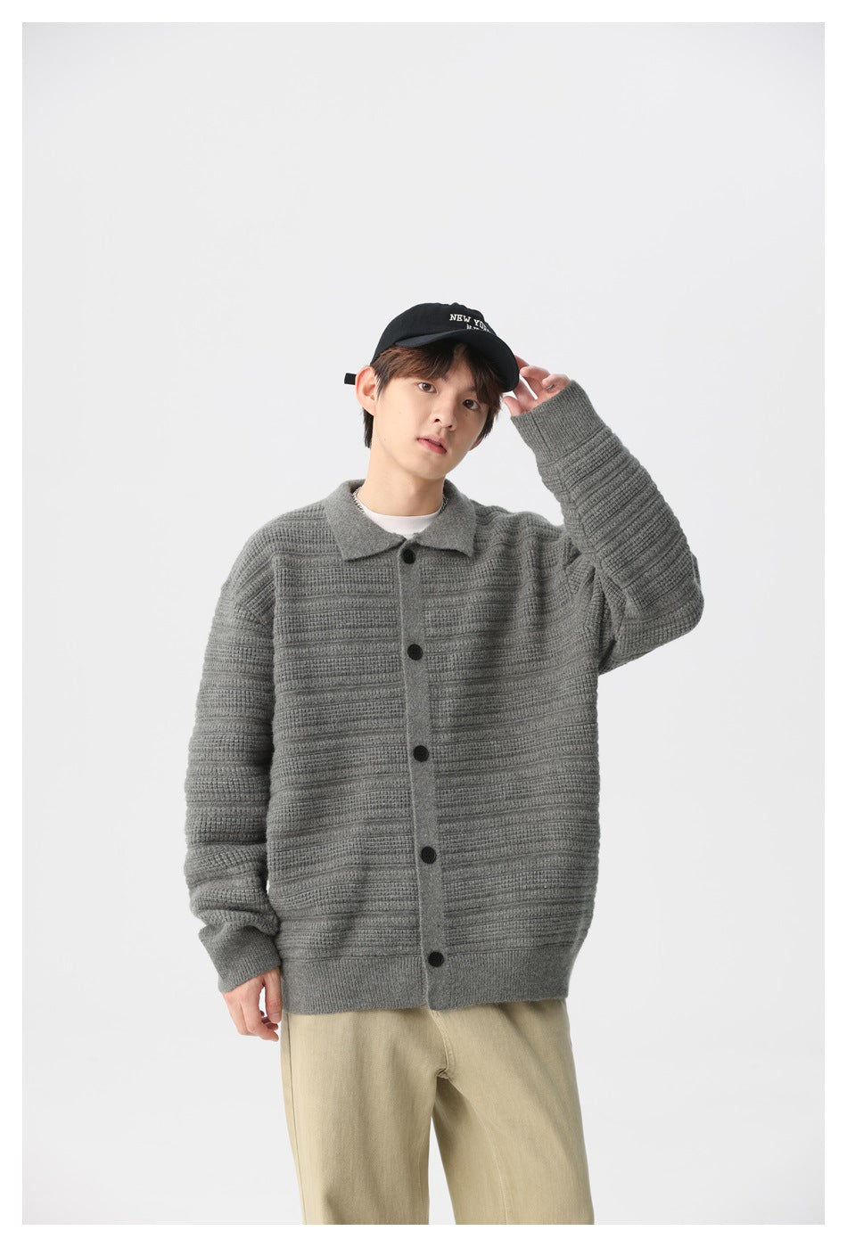 Model wearing a gray textured knit cardigan with a collar and black buttons, paired with light beige trousers.