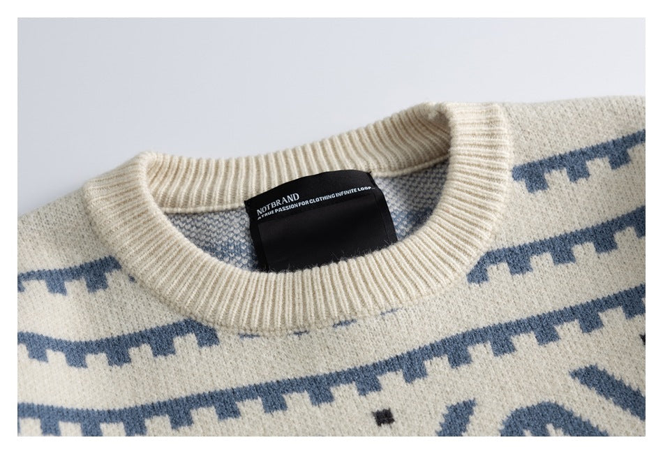 Close-up of an ivory sweater’s ribbed crew neck, blue patterning, and black sewn-in neck label.