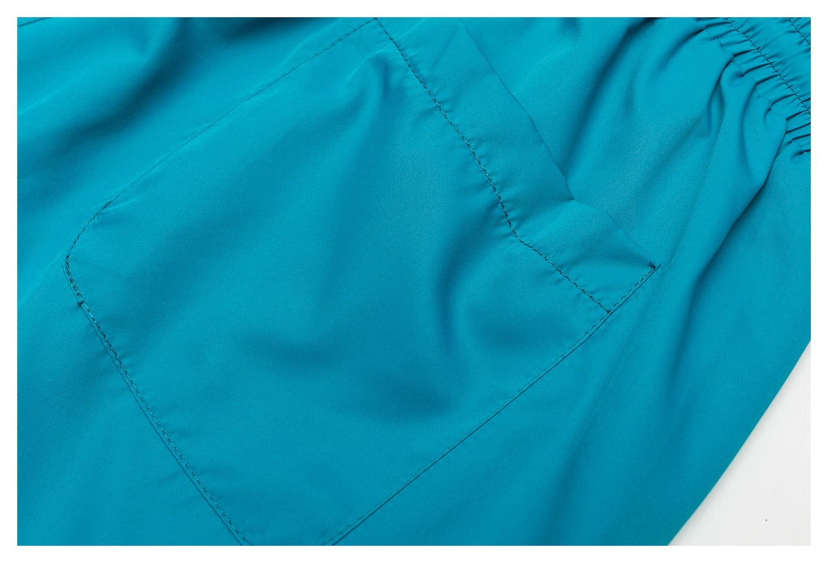 Close-up of turquoise shorts showing a large stitched patch pocket and part of the elastic waistband.
