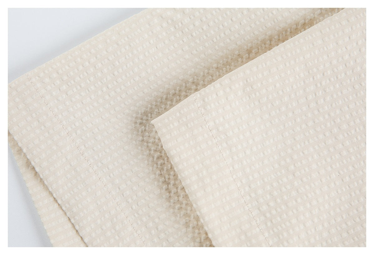 Close-up of layered off-white textured garment fabric with stitched edges and a folded cuff-like section.