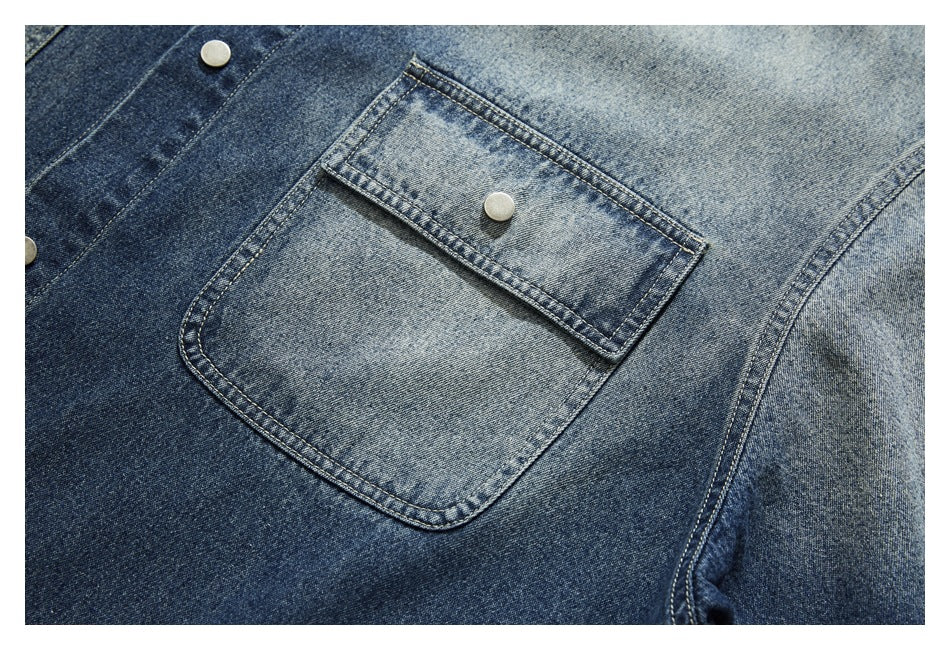 Close-up of a faded blue denim jacket pocket with a buttoned flap and visible topstitching.