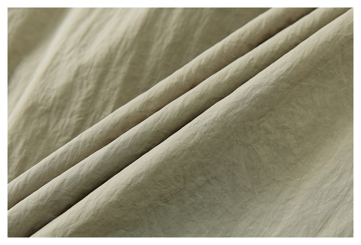 Close-up of pale beige fabric arranged in soft diagonal folds, showing its fine woven texture.
