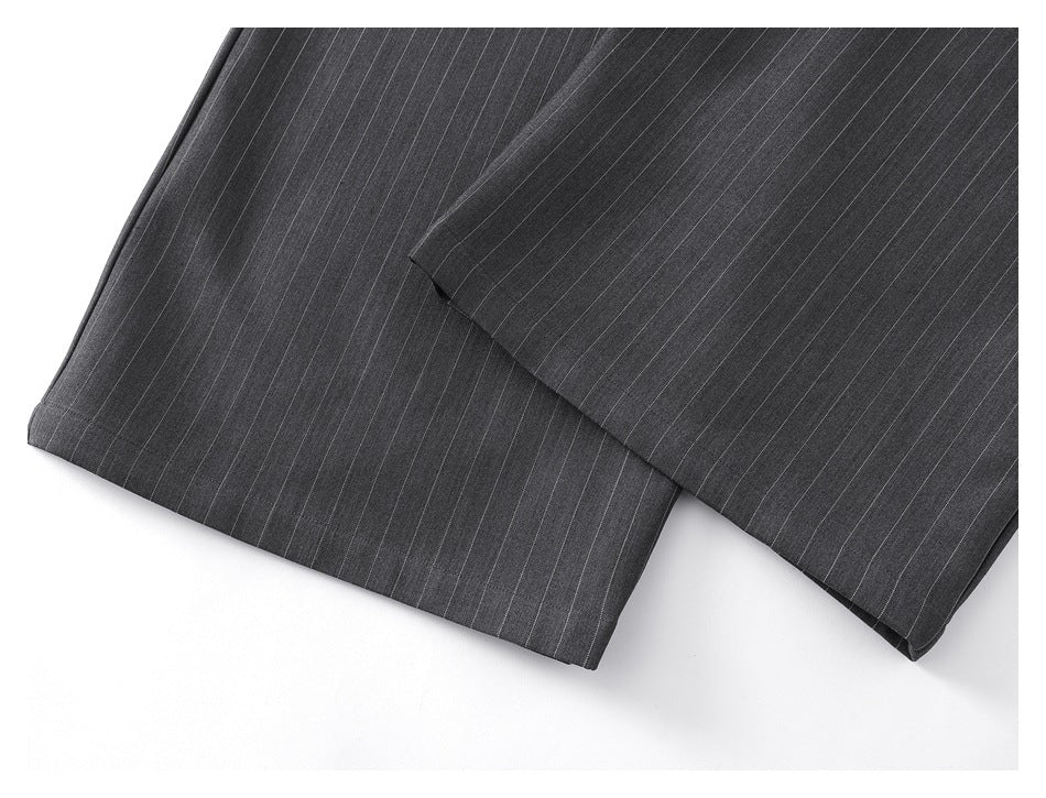 Close-up of the hems of charcoal gray trousers with thin light pinstripes.