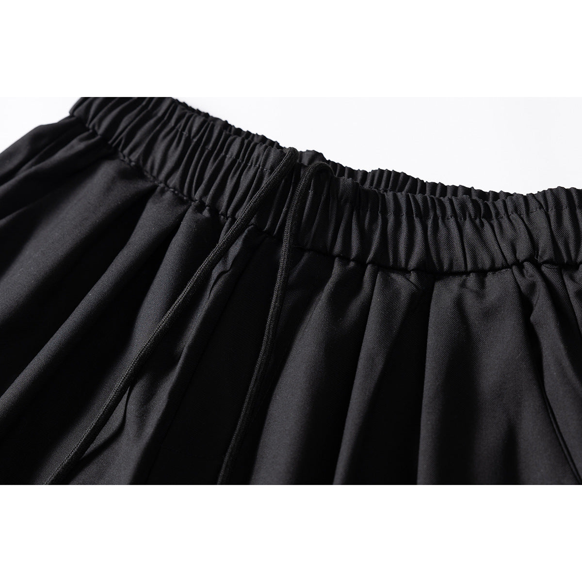 Close-up of black trousers showing a gathered elastic waistband and matching drawstring.