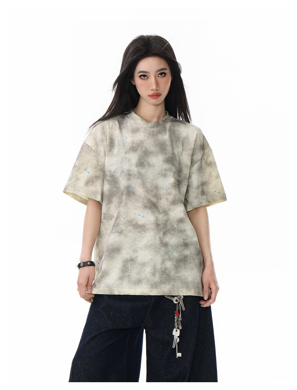 Close three-quarter view of a model wearing the beige tie-dye splatter T-shirt with dark jeans