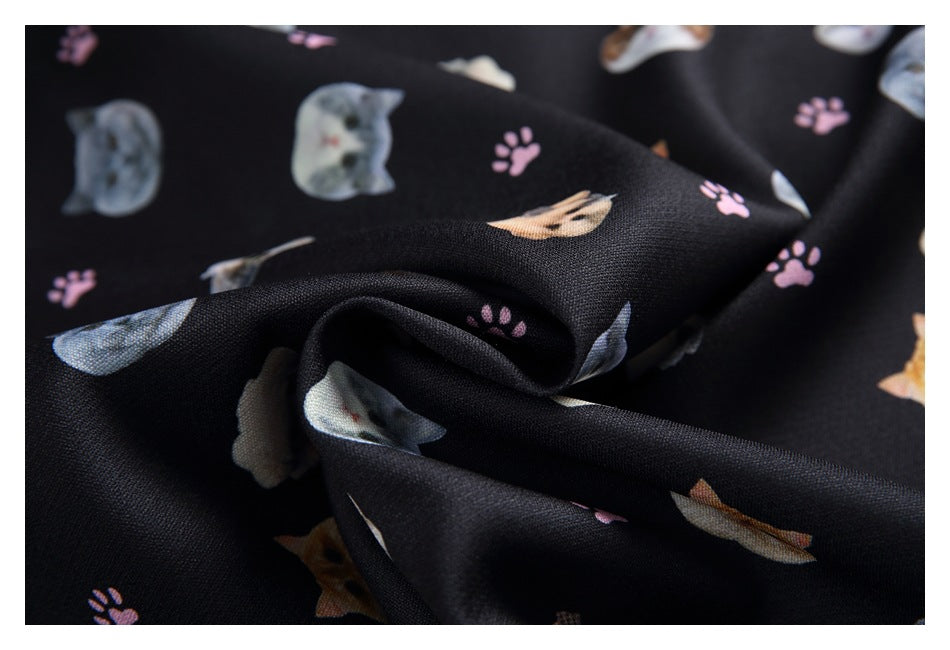 Close-up of black fabric printed with cats and pink paw prints, draped in soft folds.